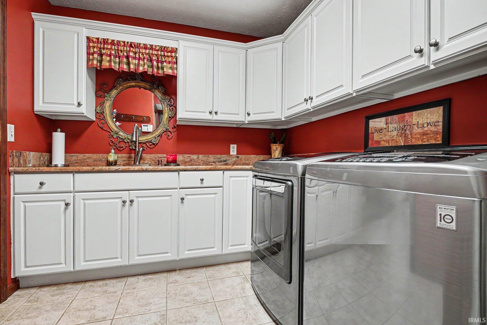 Laundry room featuring extensive white cabinetry, a single basin sink with a chrome faucet, granite-look countertops, and tile flooring