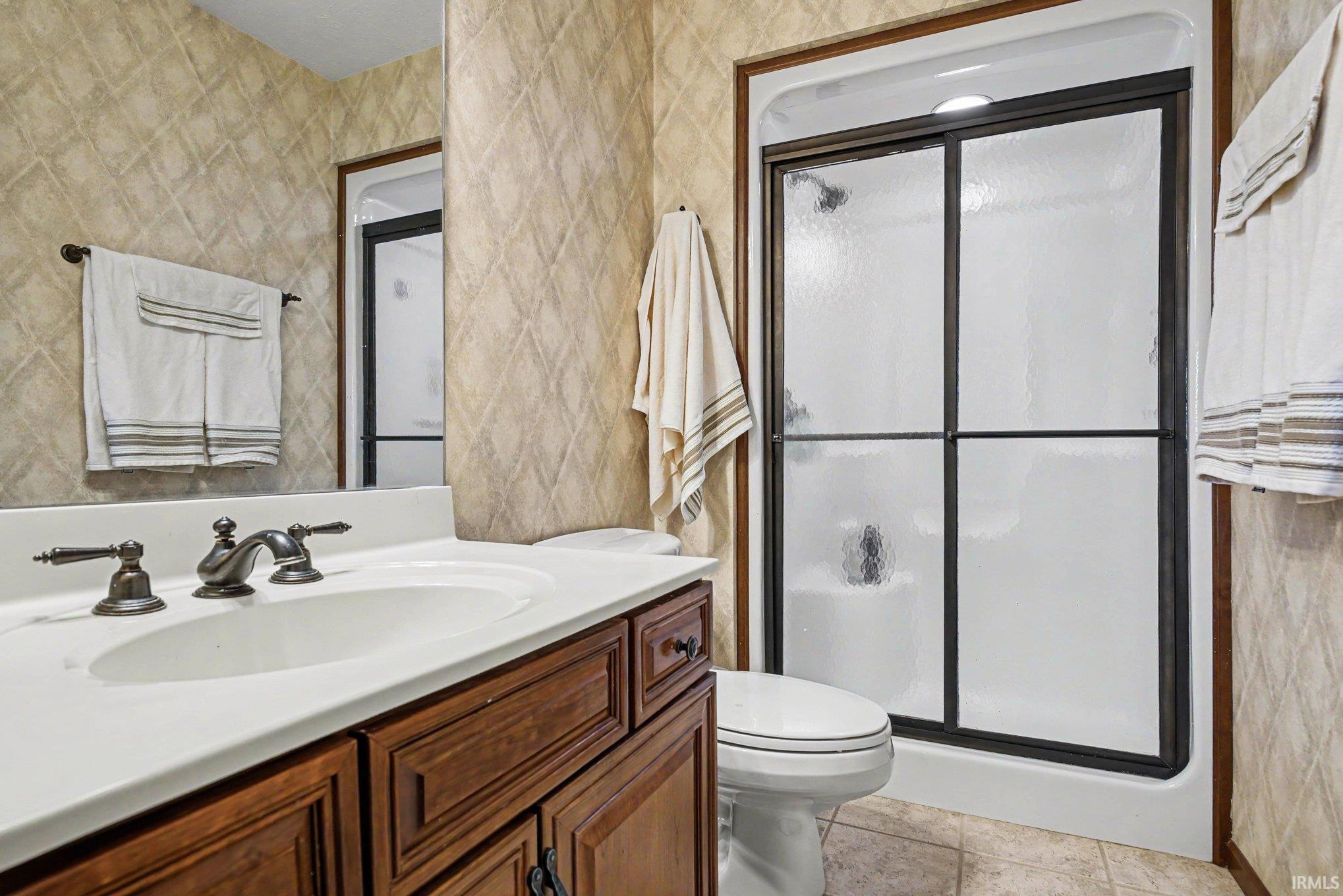 Bathroom featuring a shower with dark-framed sliding doors, a built-in vanity with a white countertop and integrated sink, dark-finished cabinetry, and textured diamond-patterned wall finishes
