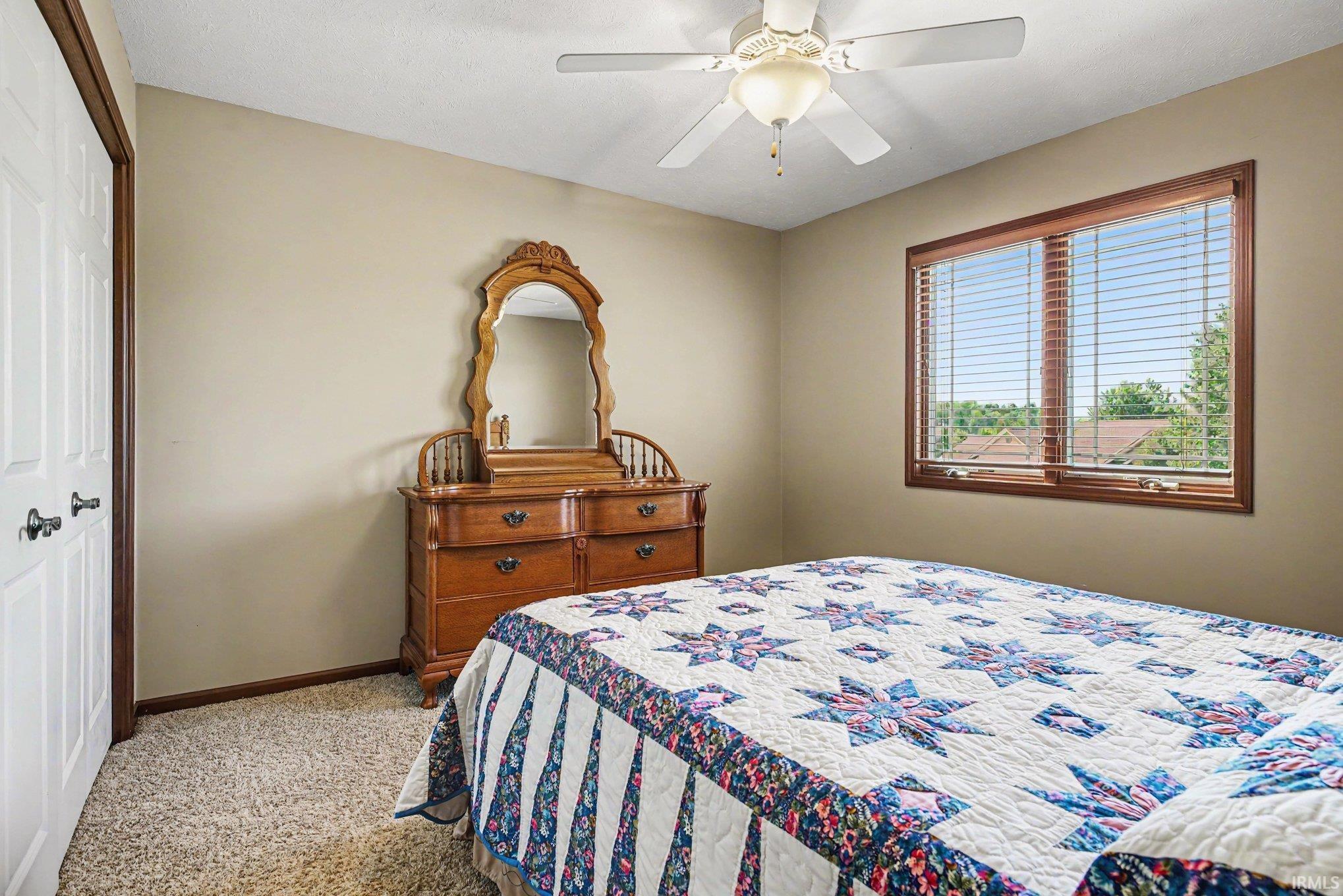 Carpeted room featuring a ceiling fan with light, a window with wood-finish trim and blinds, and a white bi-fold closet door with dark hardware