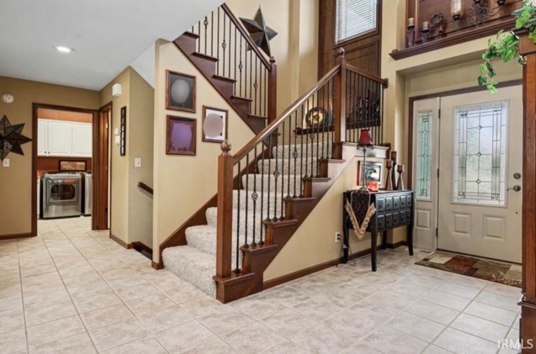 Two-story entry featuring ceramic tile flooring, a carpeted staircase with wood treads and wrought iron balusters, a front door with decorative glass inserts, and a laundry area with white cabinetry
