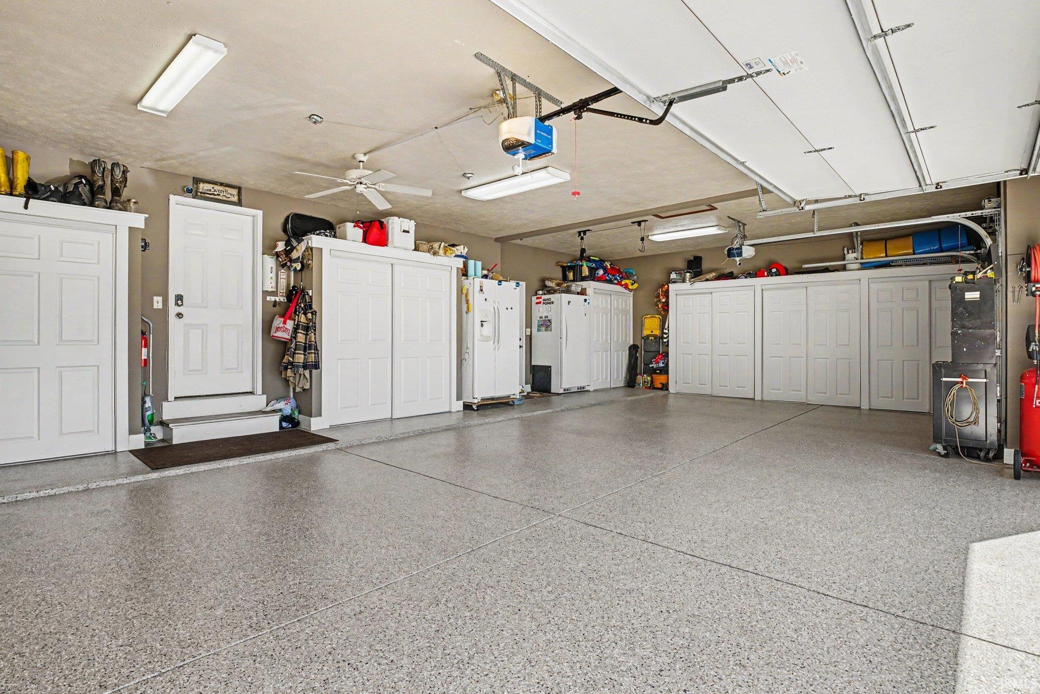 Spacious garage featuring a speckled epoxy floor, multiple white storage cabinets, two overhead garage doors with automatic openers, and fluorescent overhead lighting