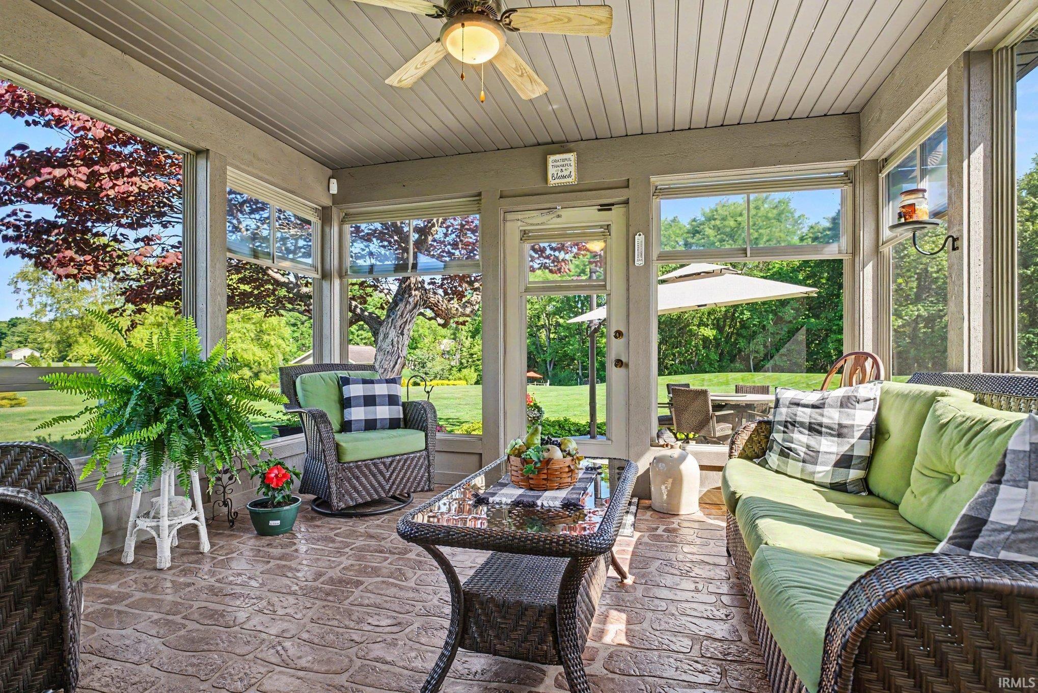 Screened porch featuring stamped concrete flooring, a wood-finish ceiling fan, and large windows providing ample natural light