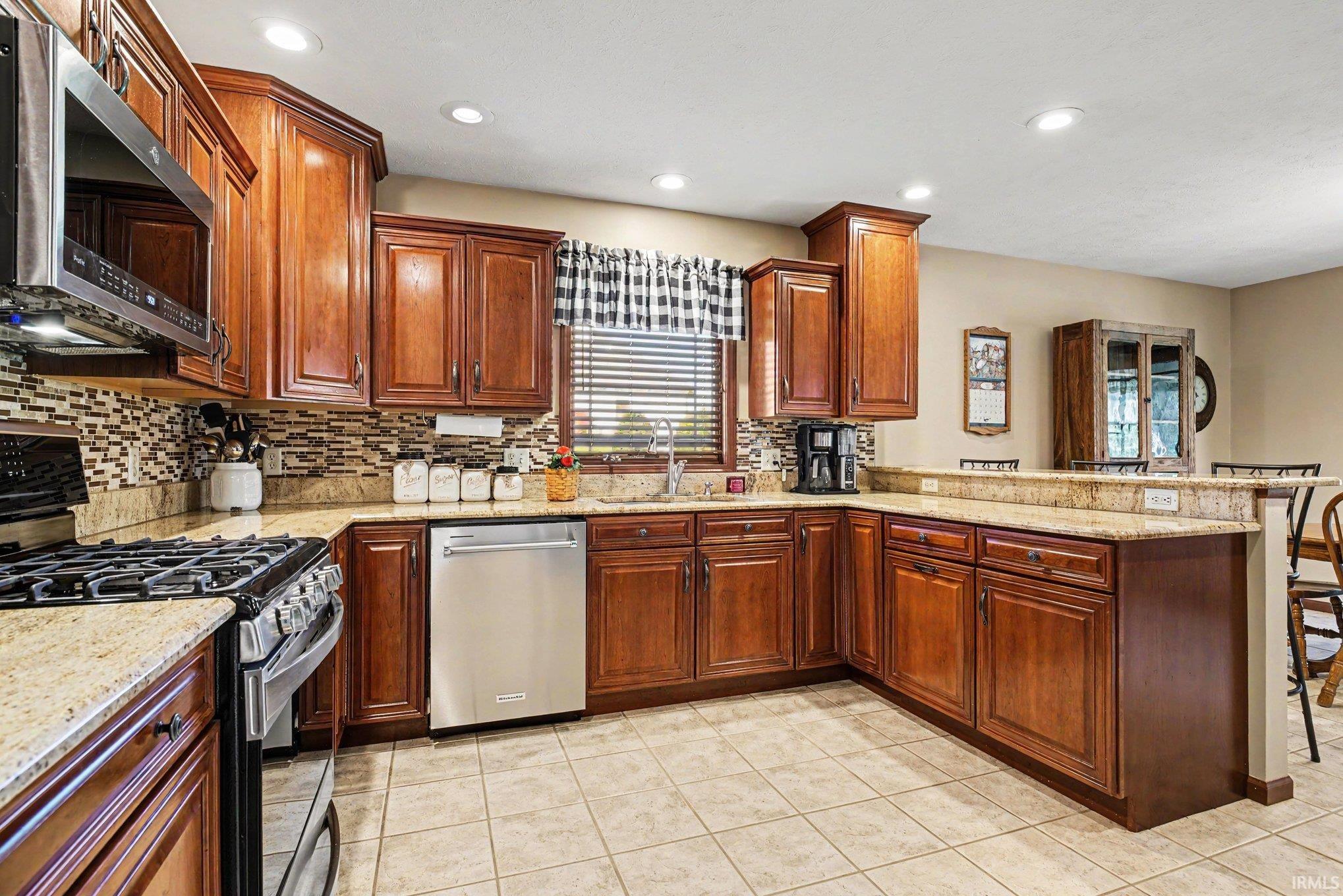 Kitchen featuring warm wood cabinetry, granite countertops, a mosaic tile backsplash, stainless steel appliances, and recessed lighting