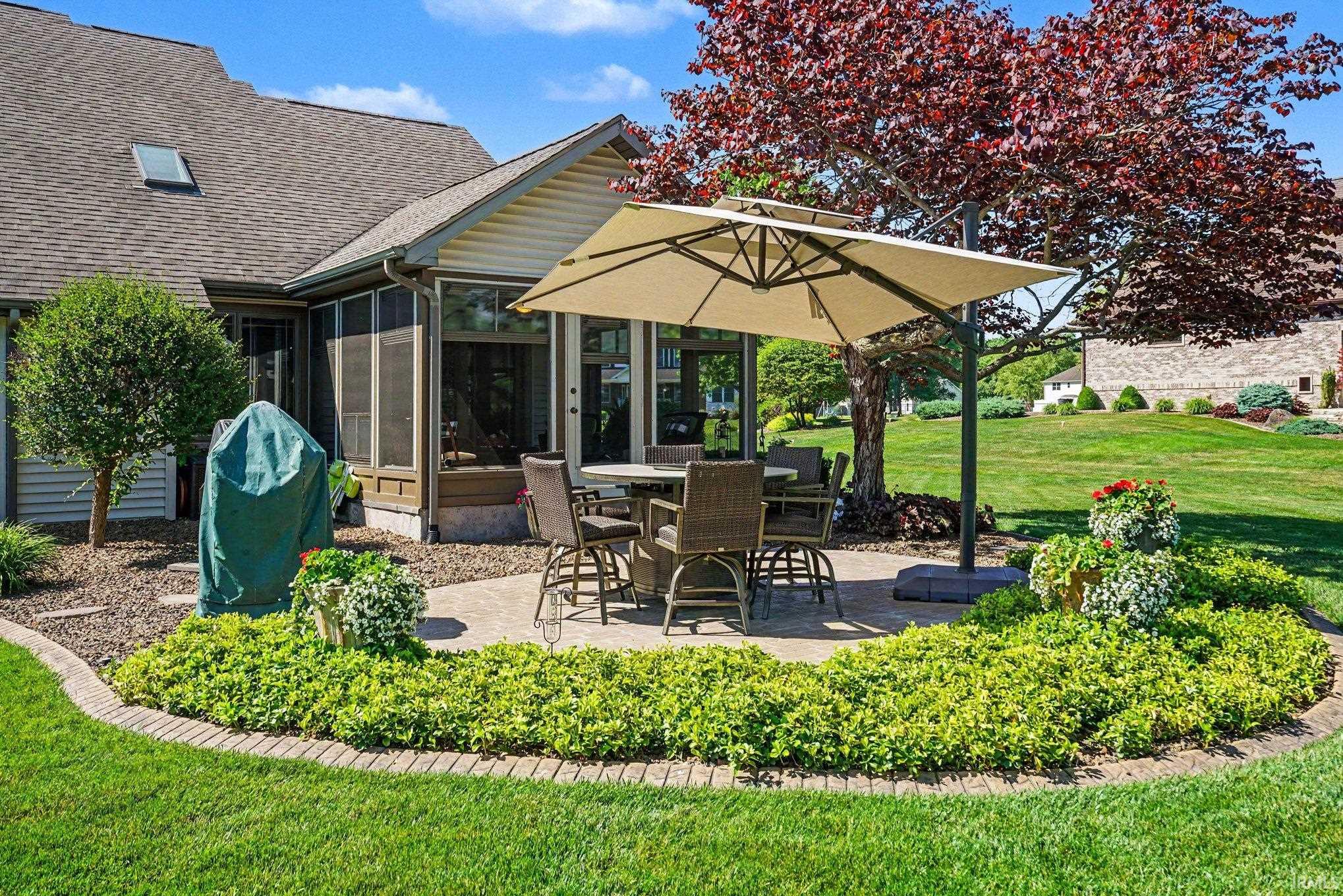 Expansive backyard featuring a paver patio with a surrounding garden bed, mature trees, and a screened-in porch