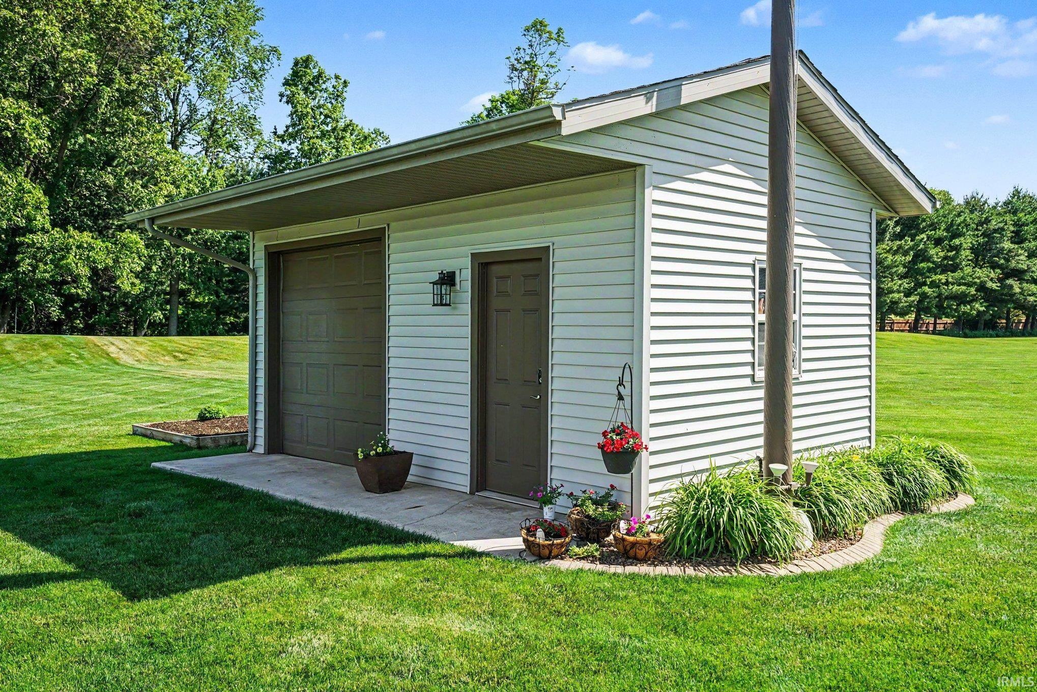 Detached structure featuring white horizontal siding, a single garage door, and a separate entry door with an exterior light fixture
