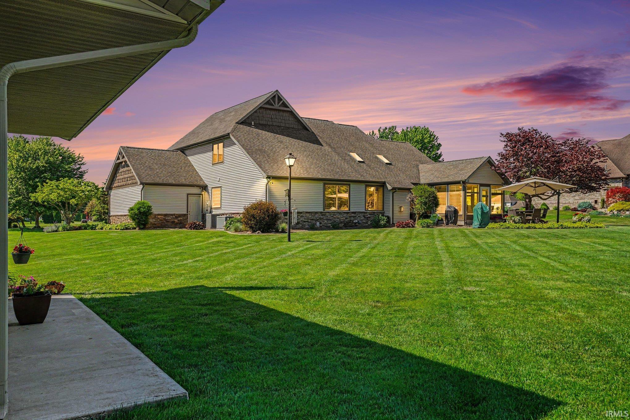 Expansive rear lawn with established landscaping, featuring a stone-clad exterior, multiple windows, and a patio area