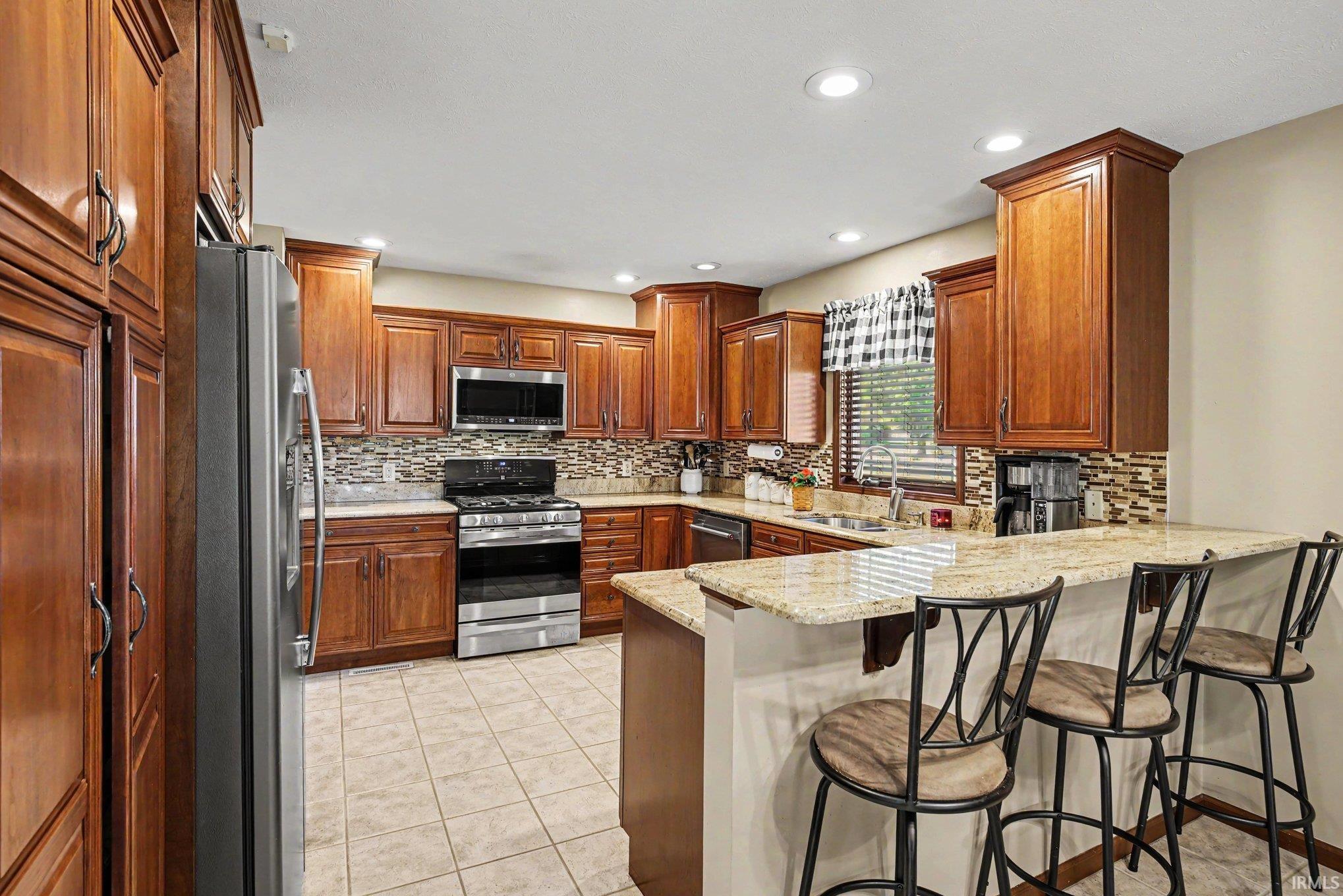 Kitchen featuring abundant wood cabinetry, stainless steel appliances, a mosaic tile backsplash, and a breakfast bar with stone countertops