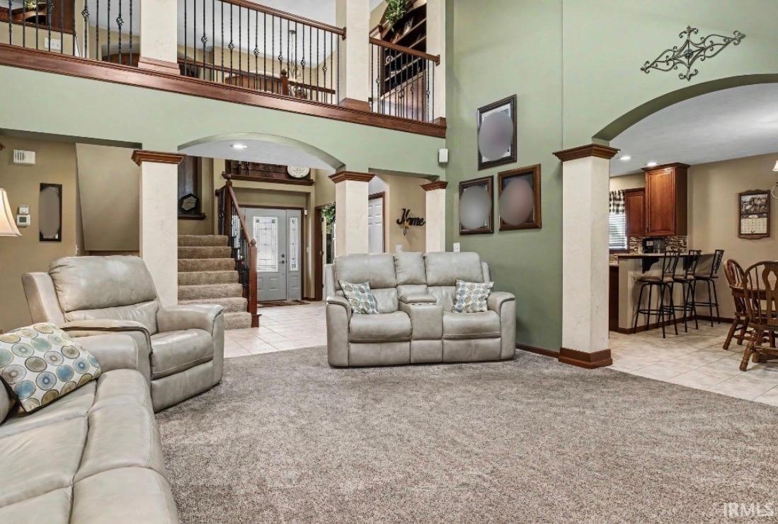 Spacious living area featuring high ceilings, a second-story overlook with wrought iron balusters, arched doorways, and a visible kitchen with wood cabinetry