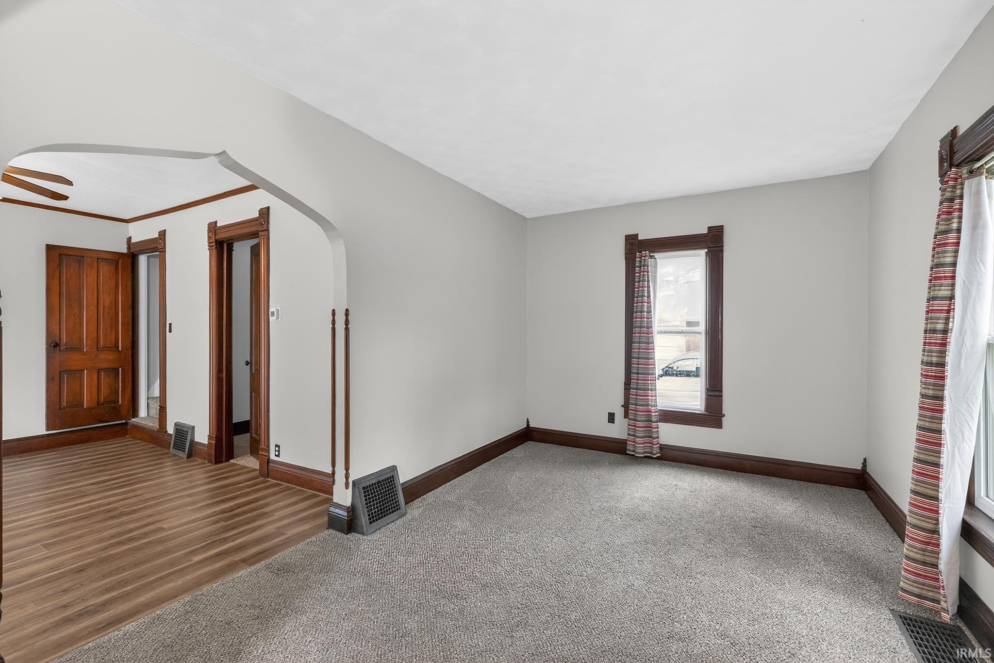 Carpeted living space featuring light gray walls, dark wood trim, and a window with wood framing