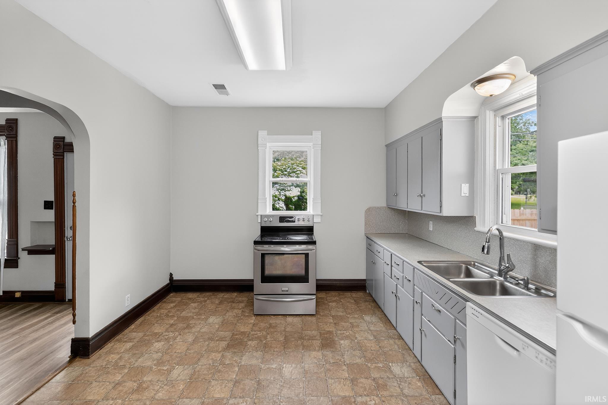 Kitchen featuring an arched doorway, patterned flooring, painted cabinetry, stainless steel range, and a double basin sink