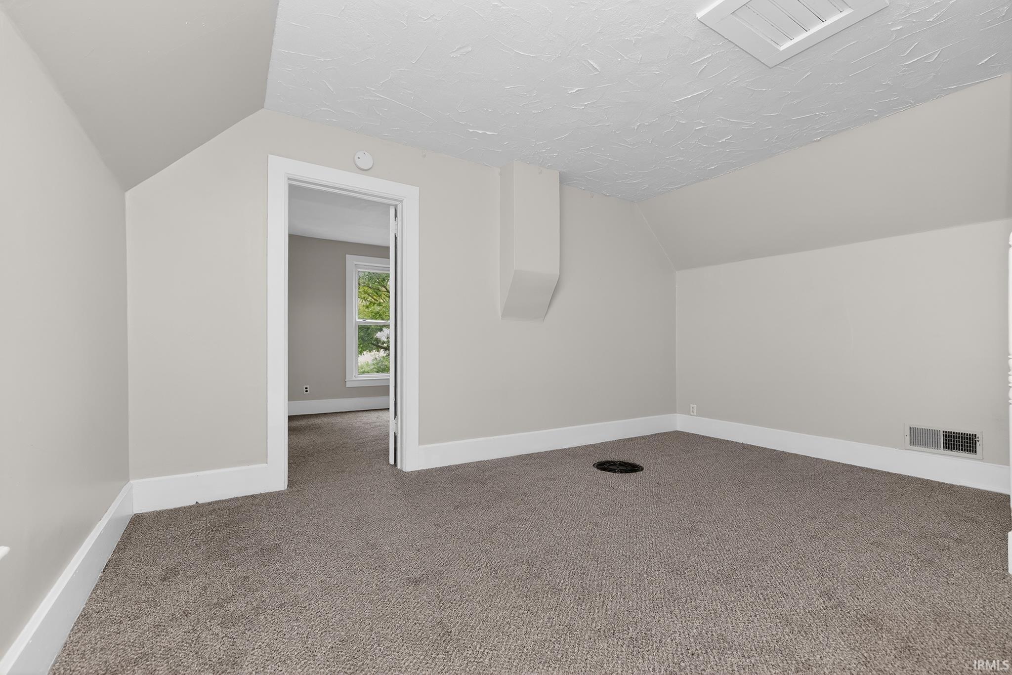 Carpeted room featuring neutral wall tones, white trim, and an attic access panel