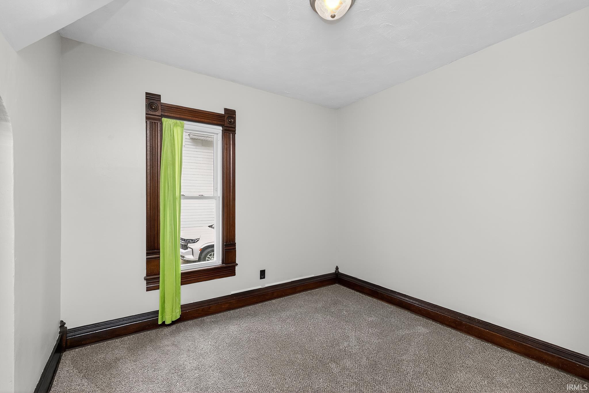 Carpeted room featuring a single window with dark wood trim, white walls, and dark wood baseboards