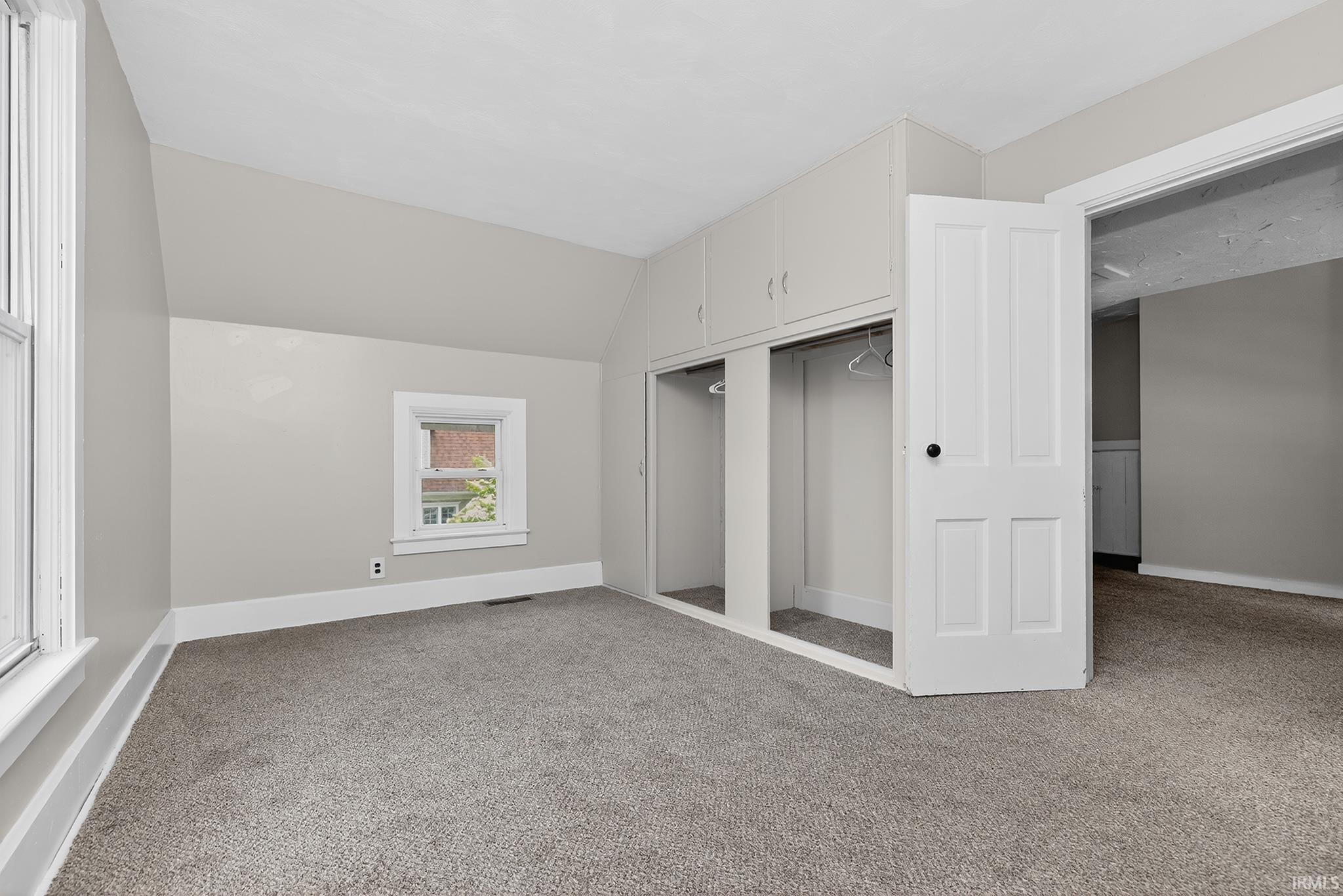 Room featuring built-in storage cabinetry, two window openings, and gray carpeting