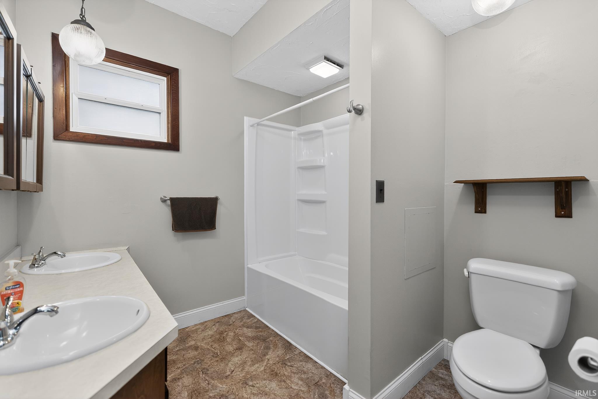 Bathroom featuring a dual-sink vanity with laminate countertop, a shower-tub combination, and a toilet
