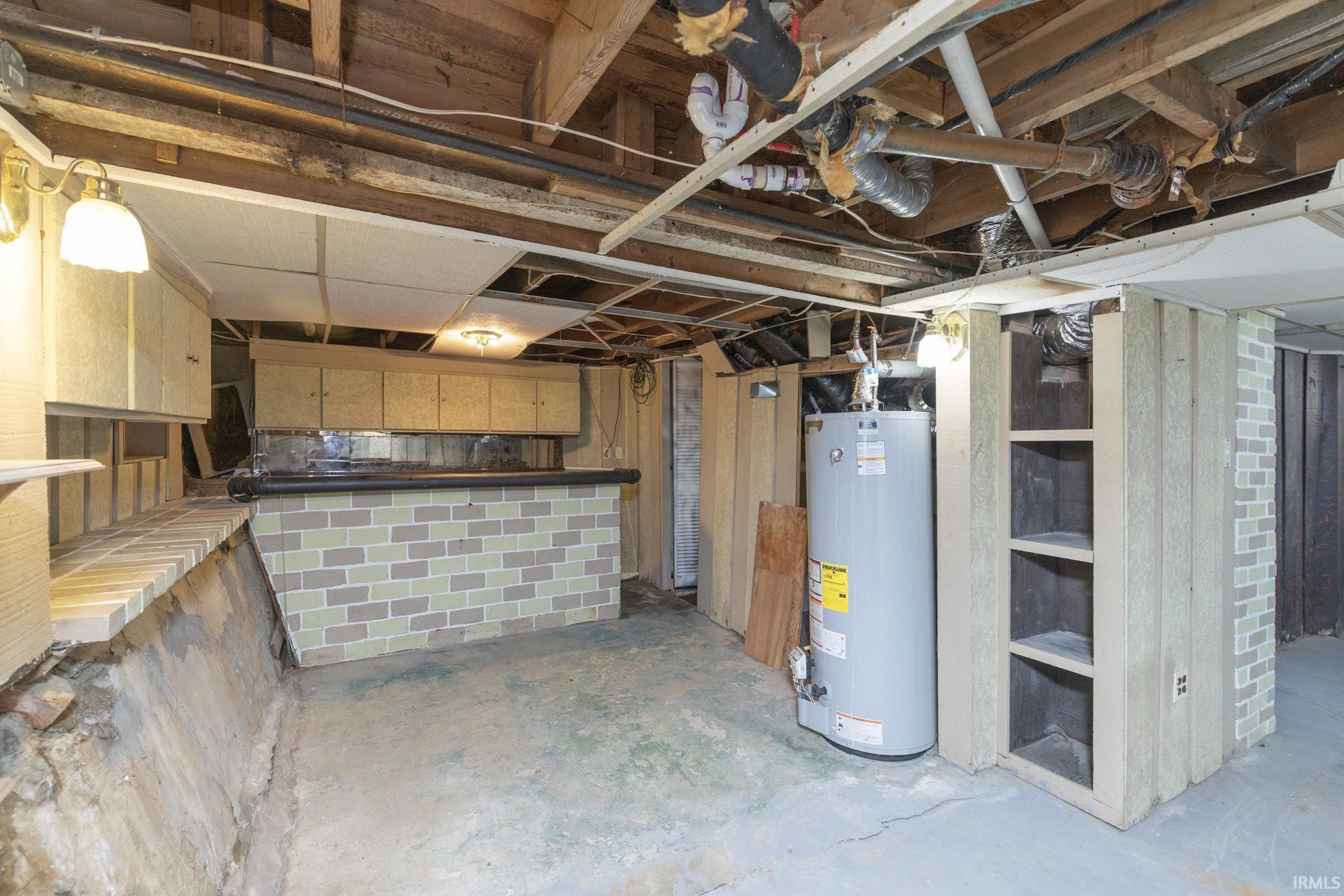 Lower level utility space featuring exposed ceiling joists, concrete flooring, and a built-in bar with brick-patterned tiling