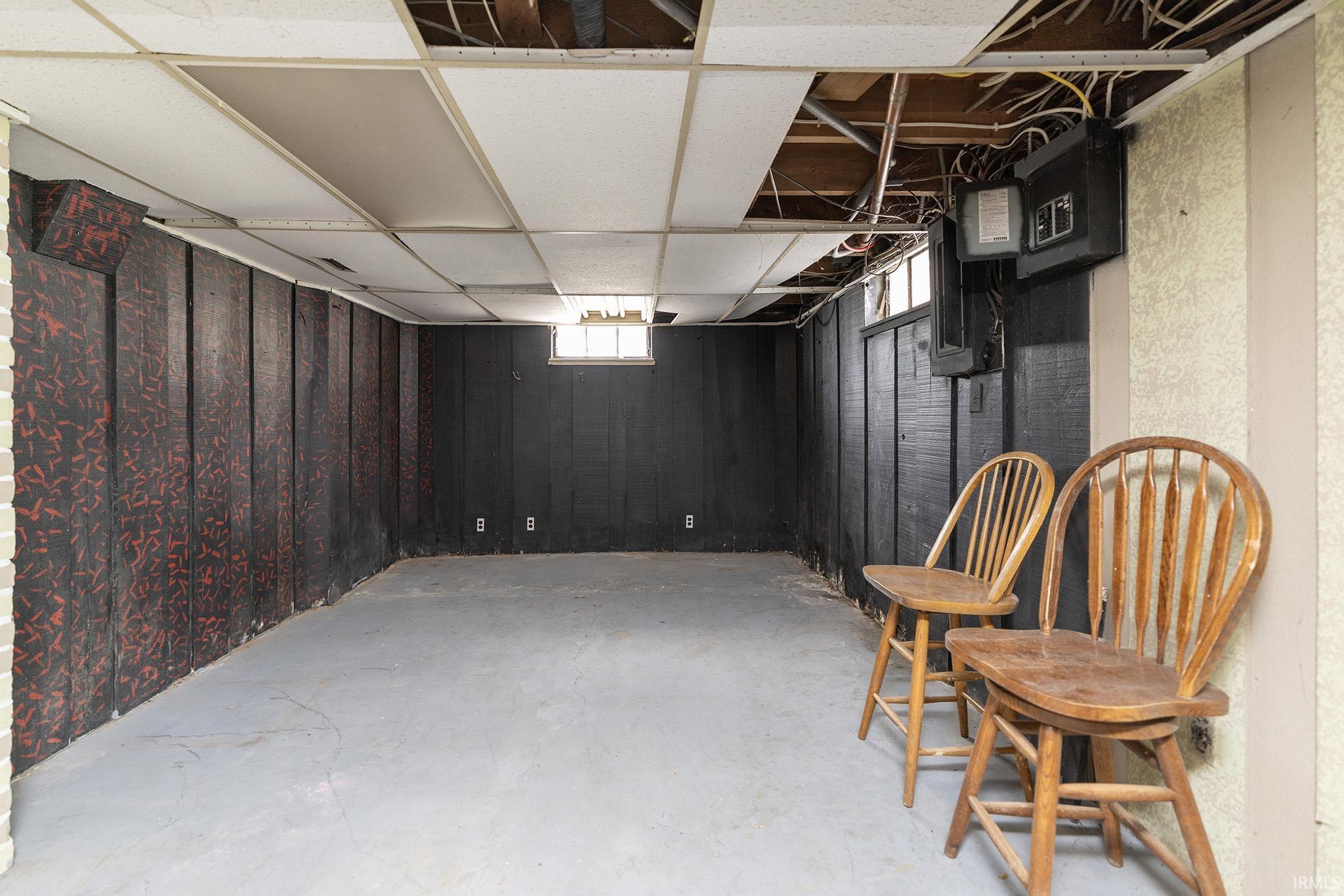 Unfinished lower level featuring a drop ceiling with exposed joists, paneling walls, and concrete flooring