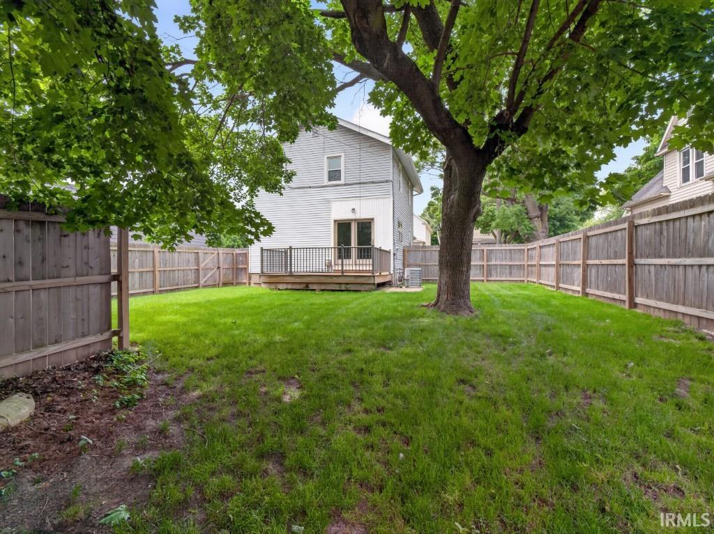 Expansive fenced backyard featuring a wood deck, mature tree, and green lawn