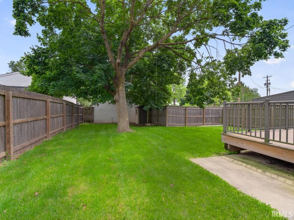 Expansive backyard featuring a mature tree, wood privacy fencing, a raised deck, and a concrete pathway