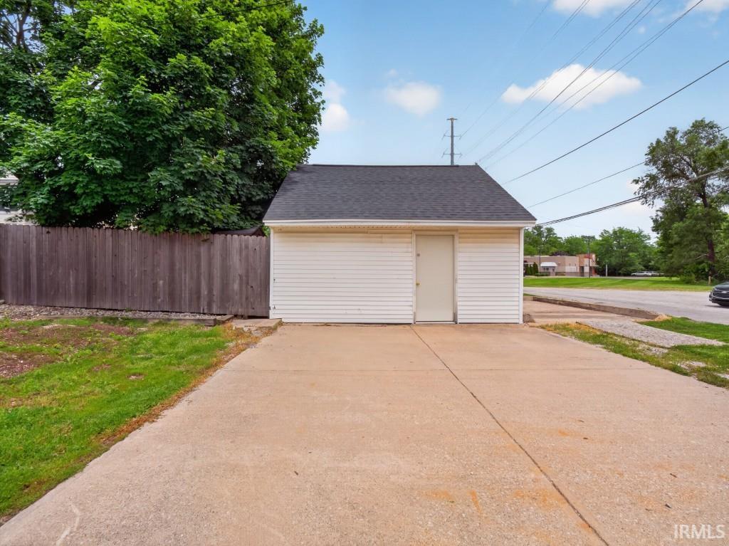 Detached garage with white vinyl siding and a dark shingle roof, featuring a pedestrian entry door and a concrete driveway