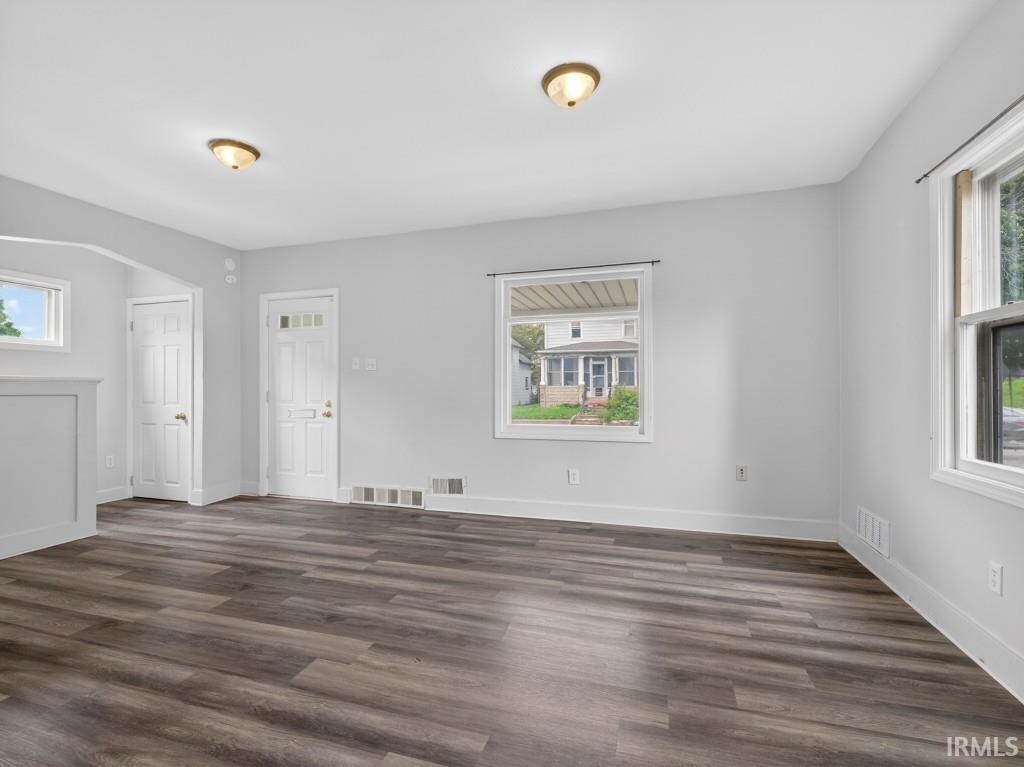Spacious room featuring wood-finish flooring, white trim, and multiple windows providing natural illumination