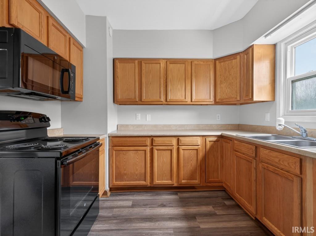 U-shaped kitchen featuring wood cabinetry, laminate countertops, a stainless steel double-basin sink, black electric range, and wood-finish flooring