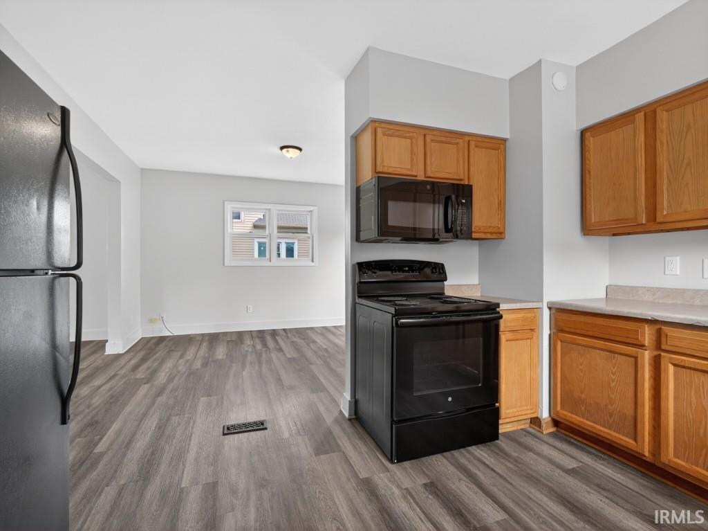 Kitchen featuring wood cabinetry, black oven range, black microwave, and light-toned countertops