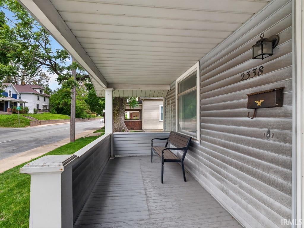 Covered front porch featuring gray siding, a wood-finish porch floor, and a white support column
