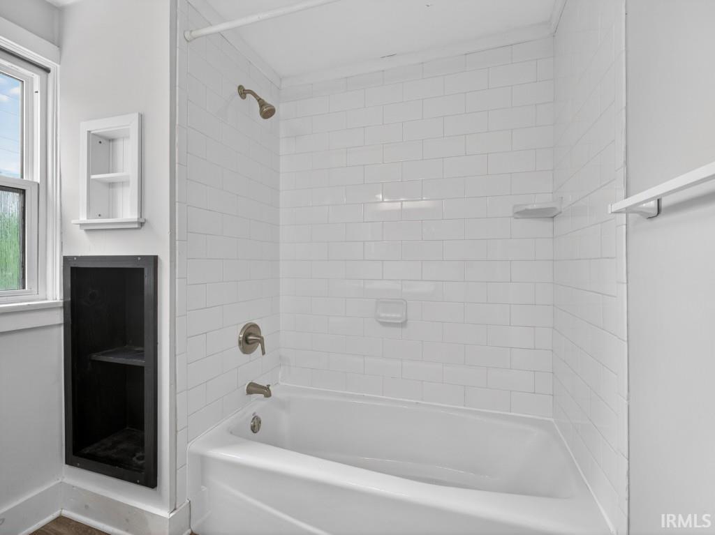 Bathroom featuring a white subway tile shower surround with a tub and brushed bronze fixtures
