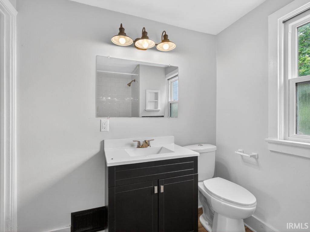Bathroom featuring a dark wood-finish vanity with an integrated white sink, a wall-mounted mirror, and a three-light fixture with bronze-tone sconces