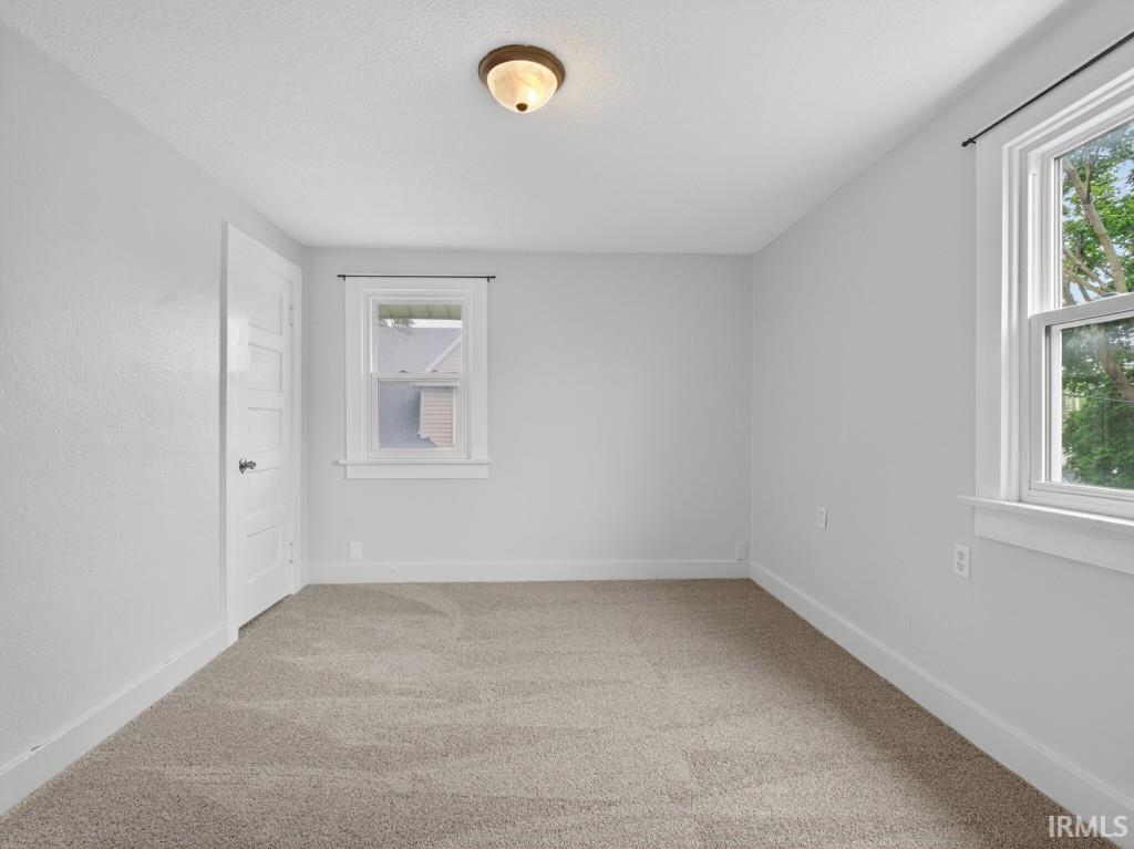 Room featuring light-colored carpeting, white baseboards, and two windows with white trim