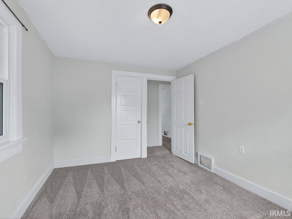 Carpeted room featuring light gray walls, white trim, and a window with white casing