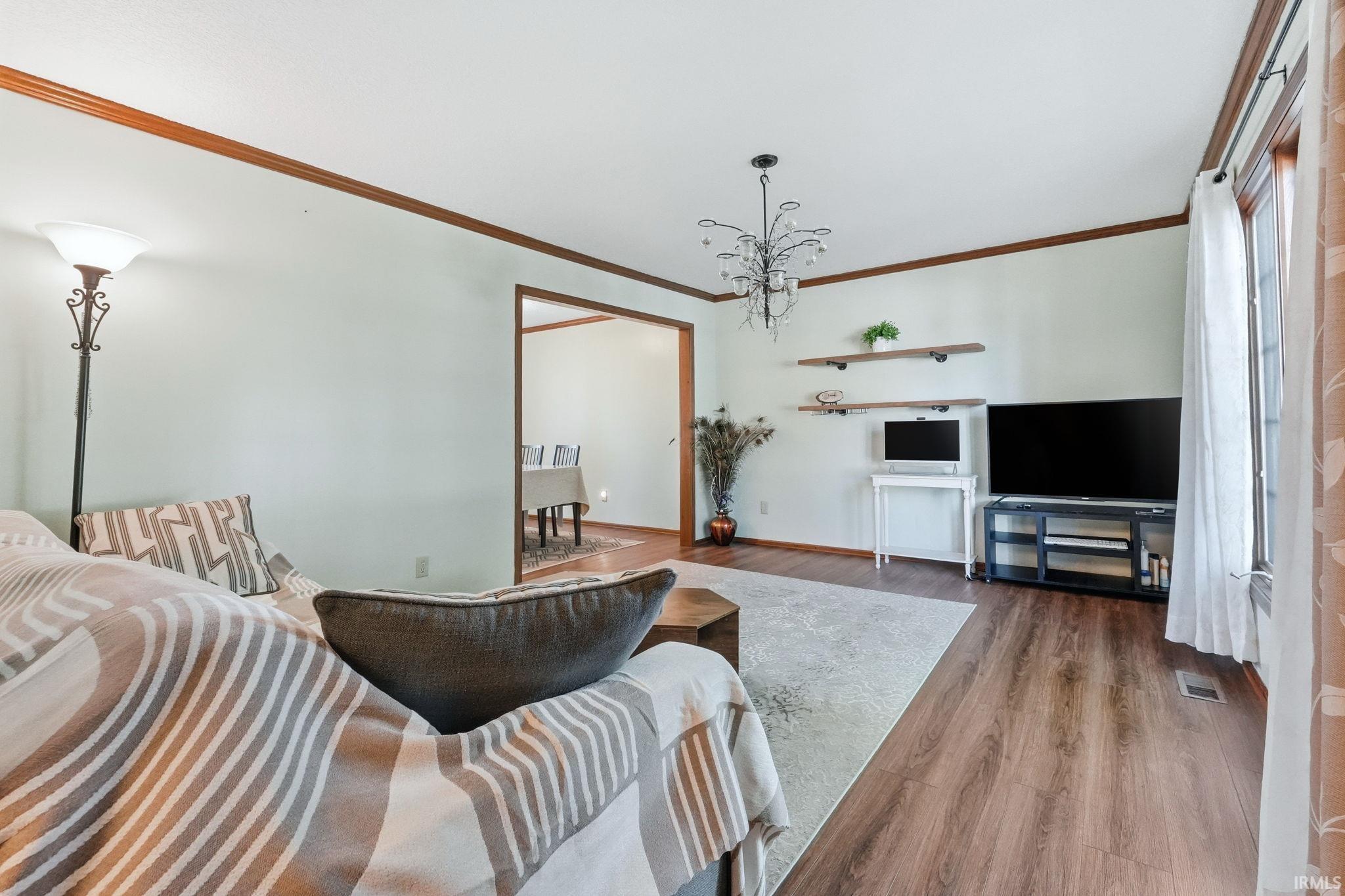 Spacious living area featuring wood-finish flooring, a decorative chandelier, and an open doorway to an additional room