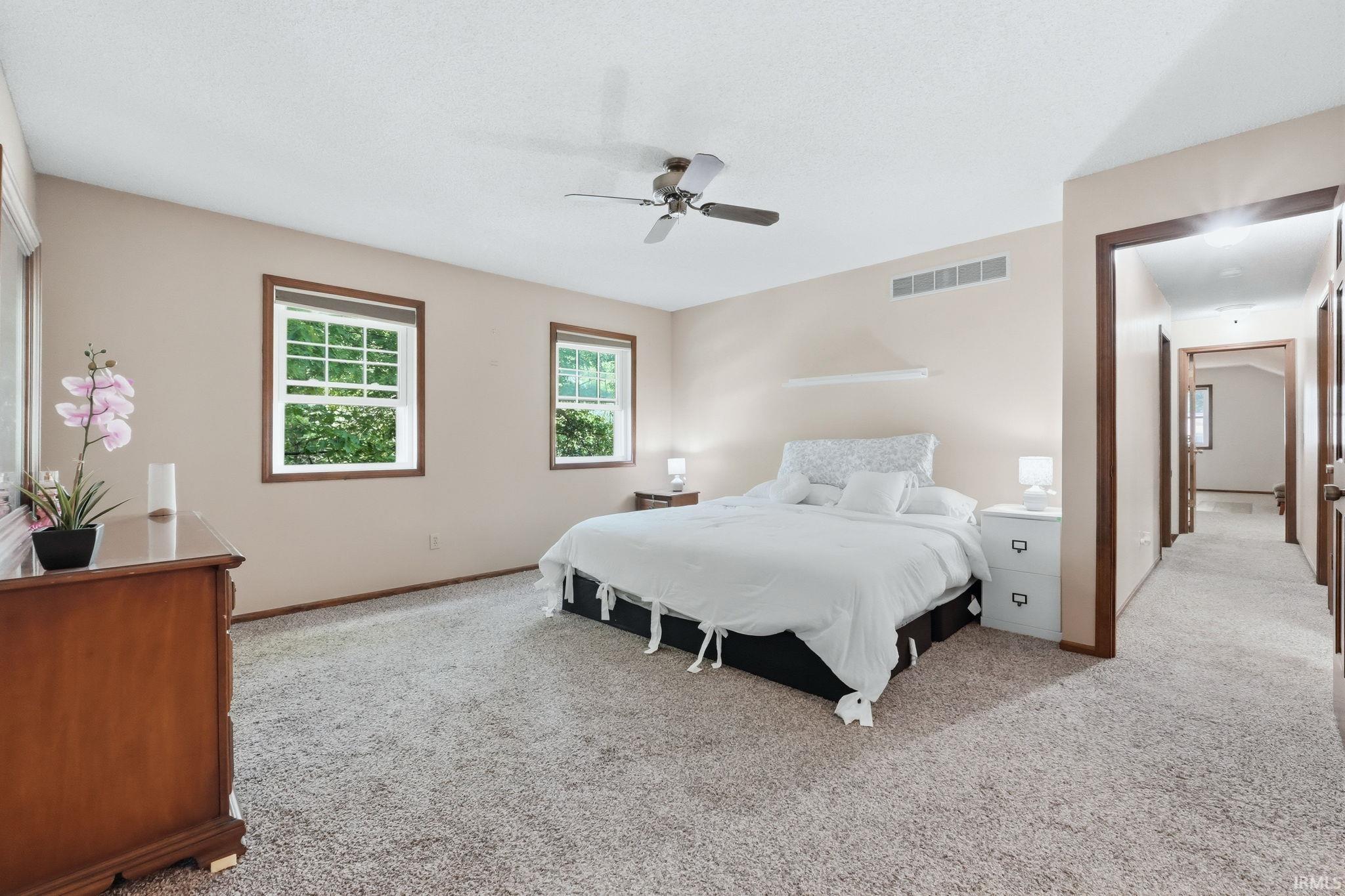 Bedroom featuring neutral-toned carpeting, two windows with dark wood trim, and a ceiling fan