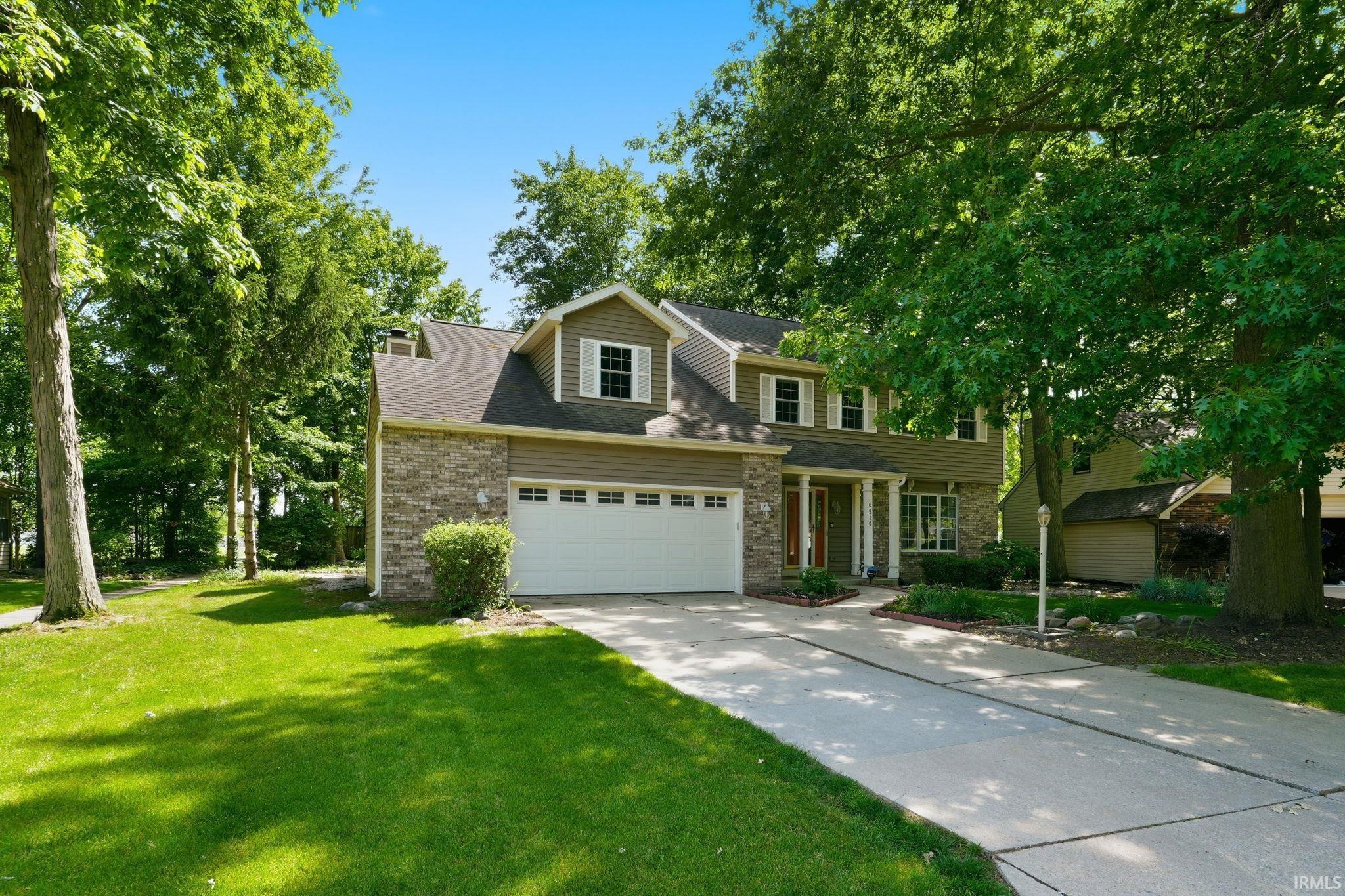 Two-story residence featuring a two-car garage, stone and siding exterior, a concrete driveway, and mature landscaping