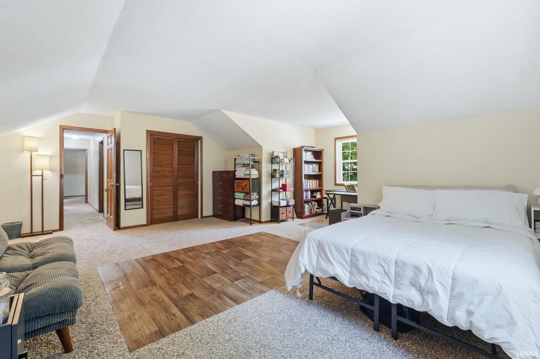 Spacious room featuring carpeting with a wood-finish flooring insert, a window, and sloped ceilings