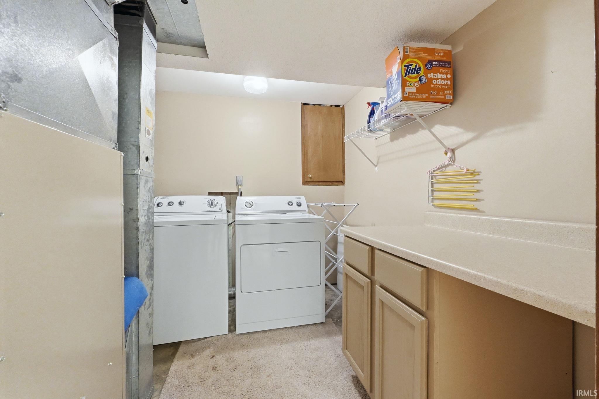 Laundry area featuring a pair of white appliances, built-in lower cabinetry, a light-colored countertop, and a wall-mounted shelving unit