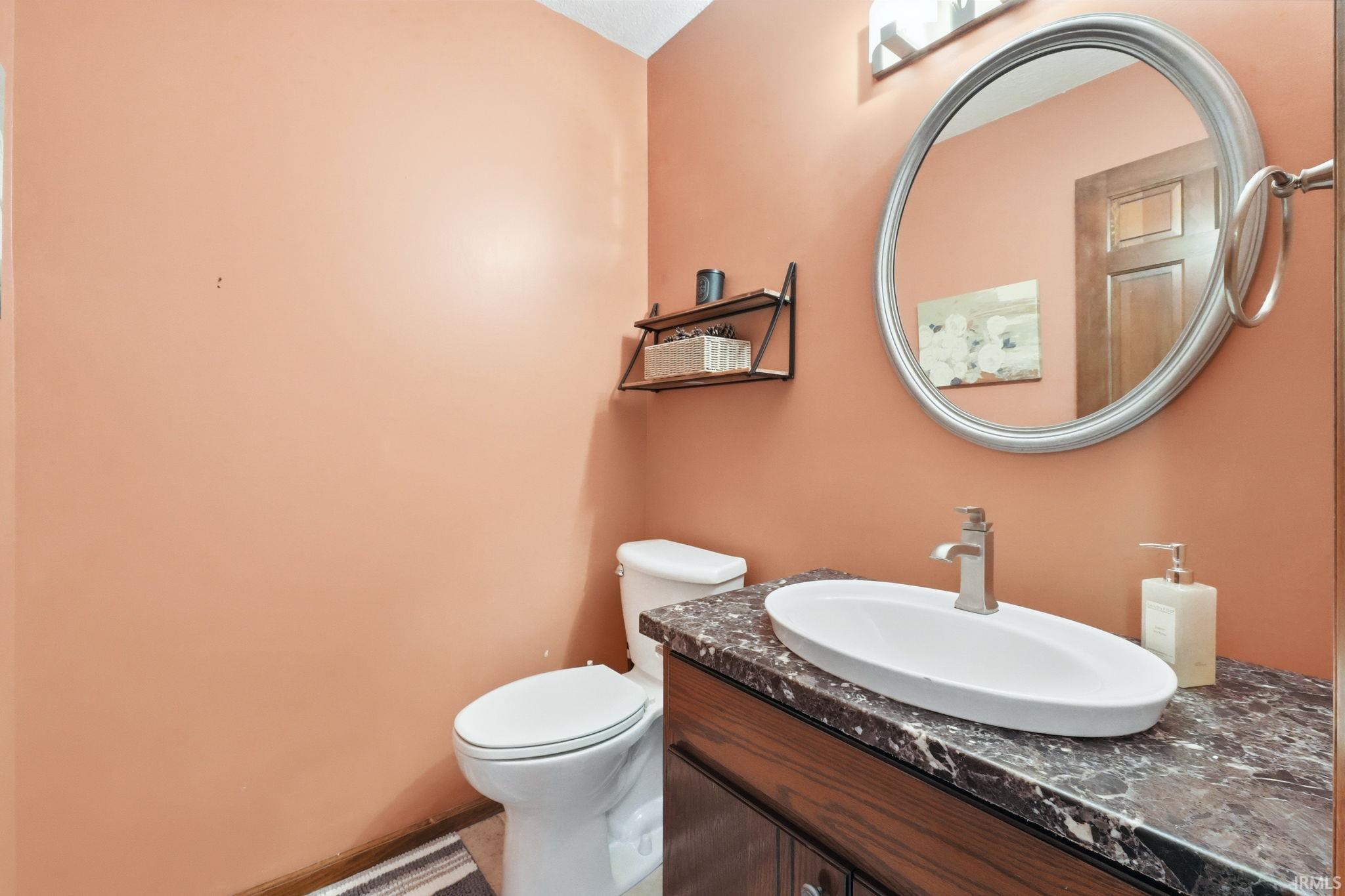 Powder room featuring a vessel sink, vanity with dark wood-finish cabinetry, a circular mirror with a silver-toned frame, and wall-mounted shelving