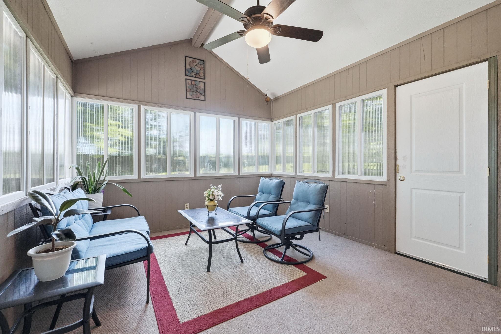 Sunroom featuring a vaulted ceiling with a ceiling fan, multiple windows, and a panel door