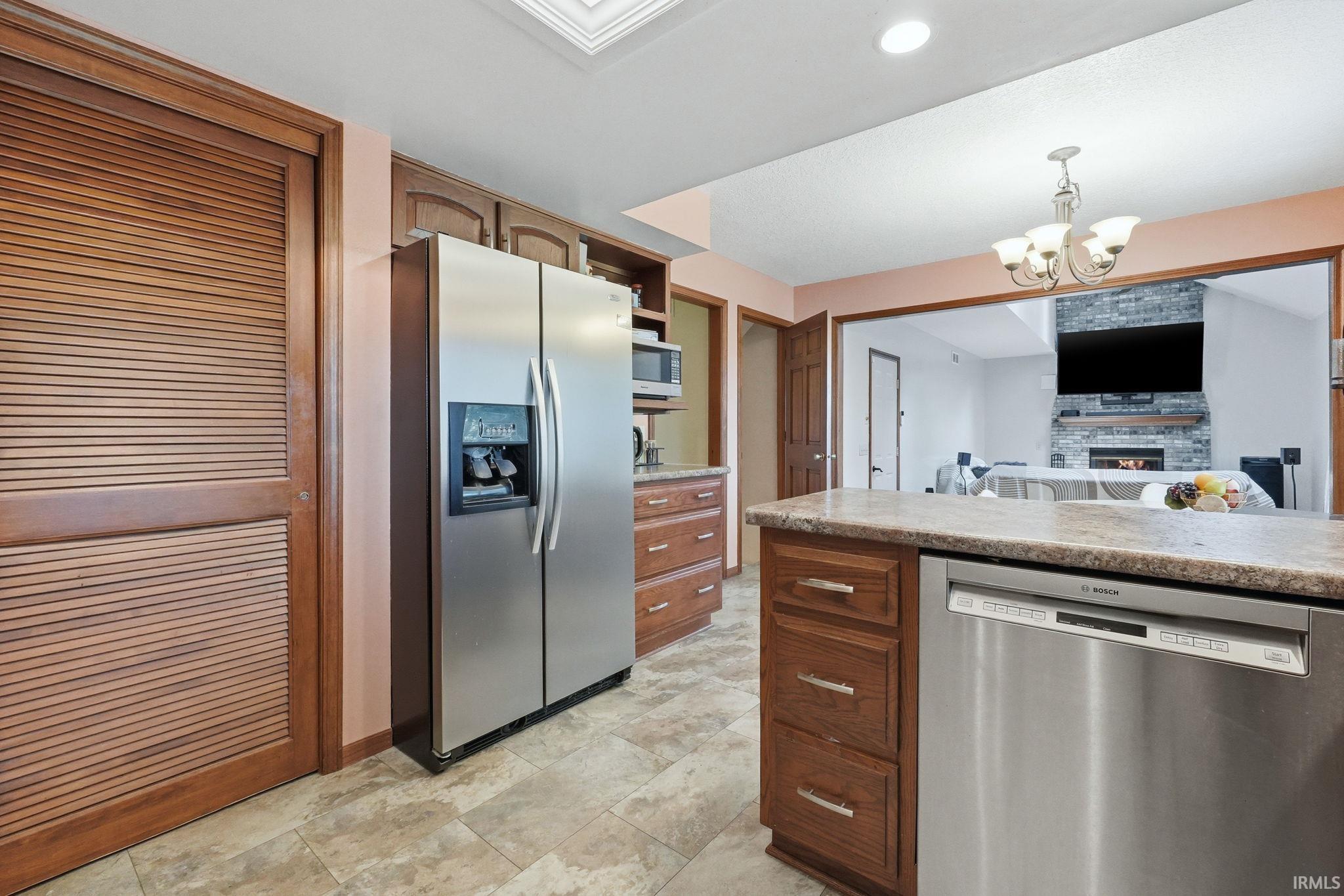 Kitchen featuring a stainless steel side-by-side refrigerator, under-counter dishwasher, wood cabinetry, and a stone-finish countertop