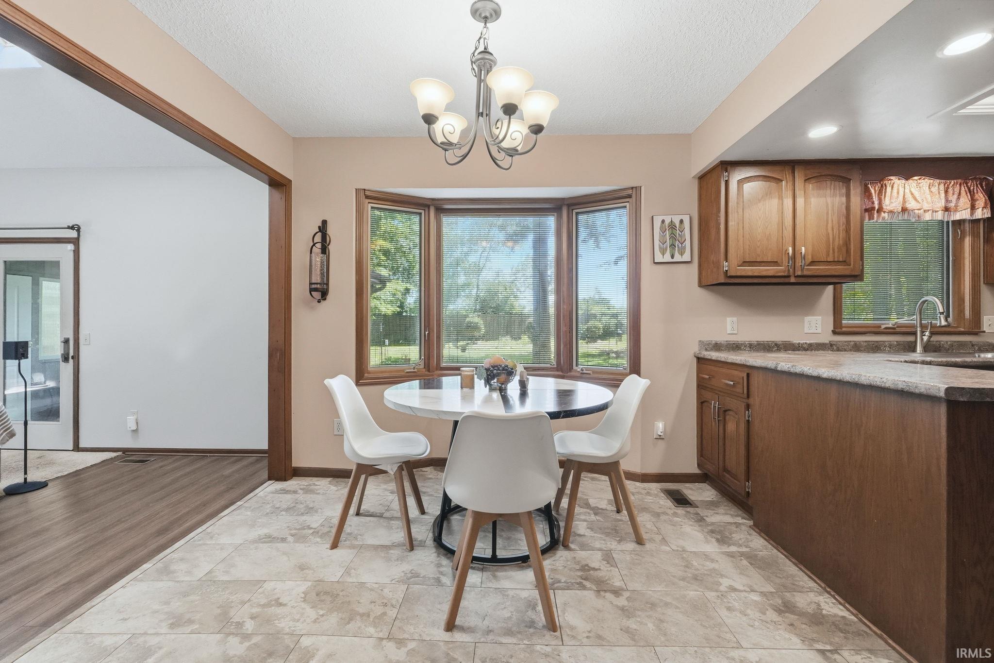 Kitchen dining area featuring a bay window, wood-finish cabinetry, a stainless steel sink, and durable tile flooring