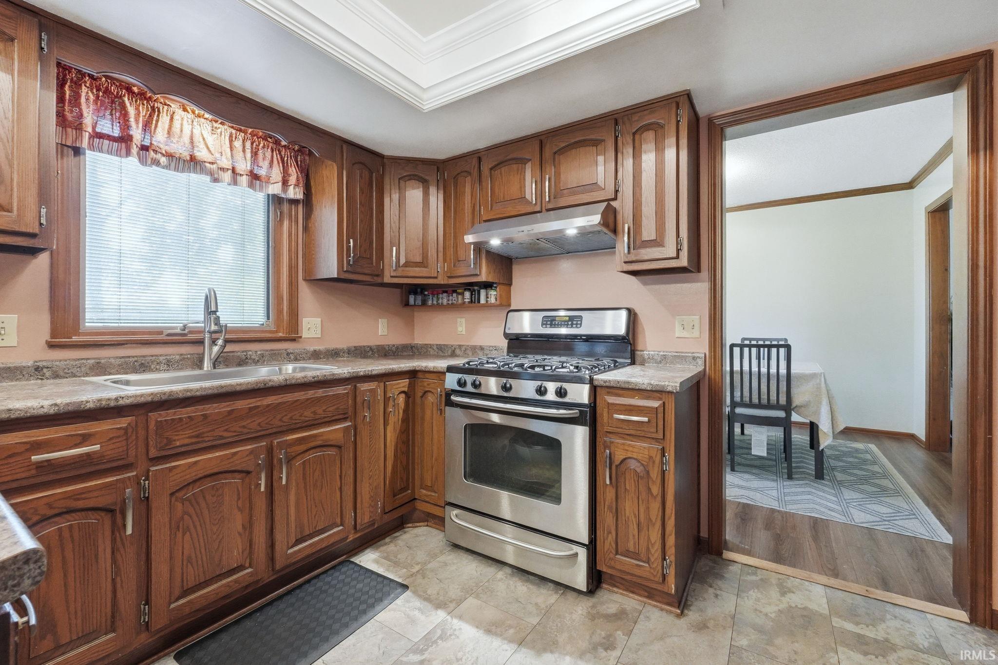 Kitchen featuring wood cabinetry, stainless steel range, and a window with blinds