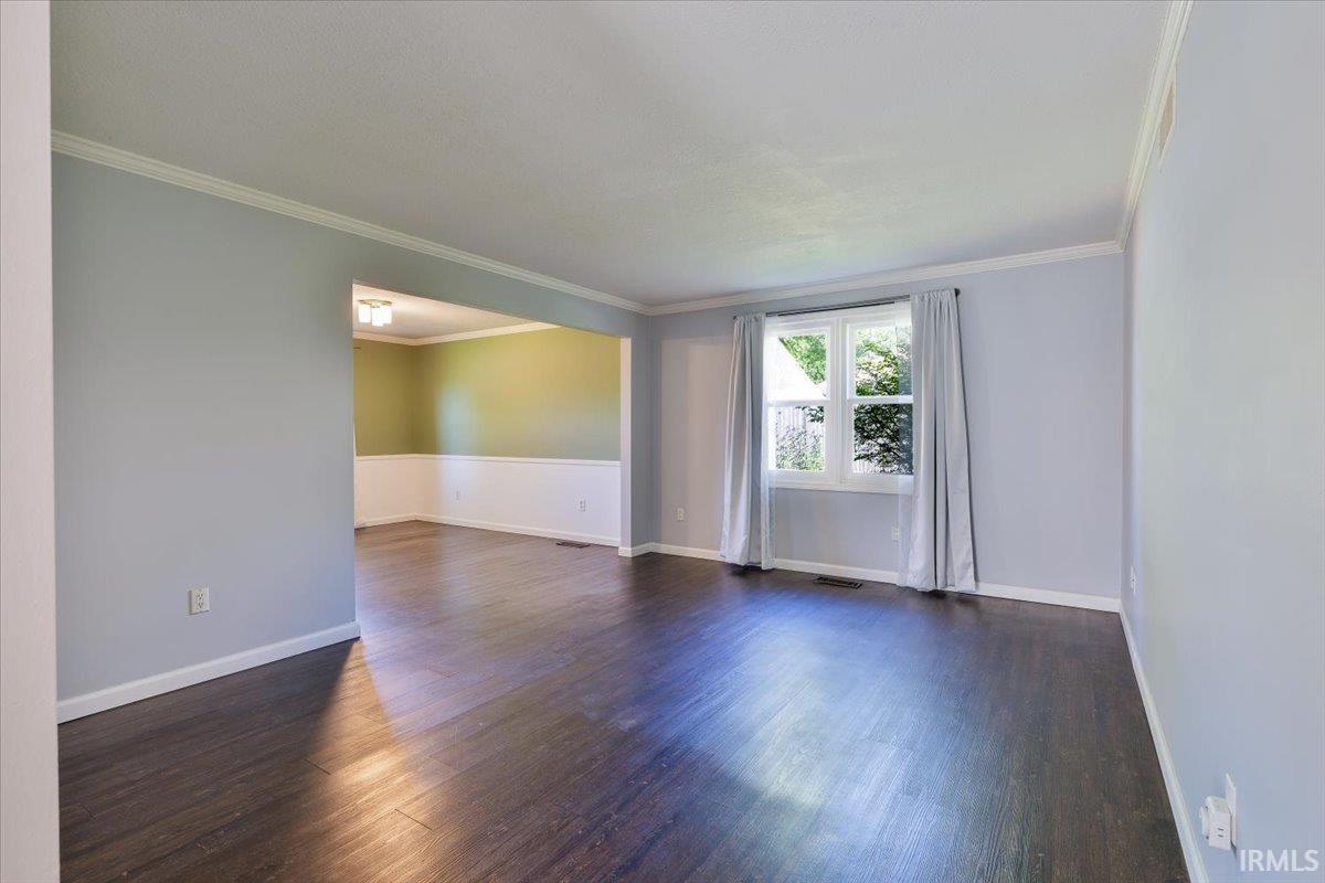 Open-concept living area featuring dark wood-finish flooring, light blue walls, and white crown molding