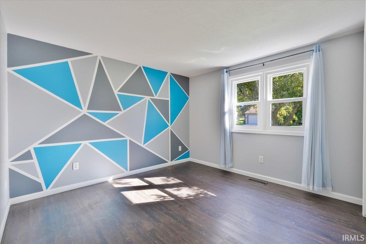 Room featuring a geometric accent wall in shades of blue and gray, wood-finish flooring, and a double window with white trim