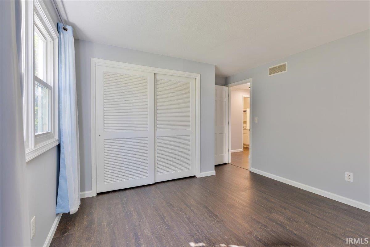 Bedroom featuring wood-finish flooring, light gray walls, a window with white trim, and a closet with white louvered bifold doors