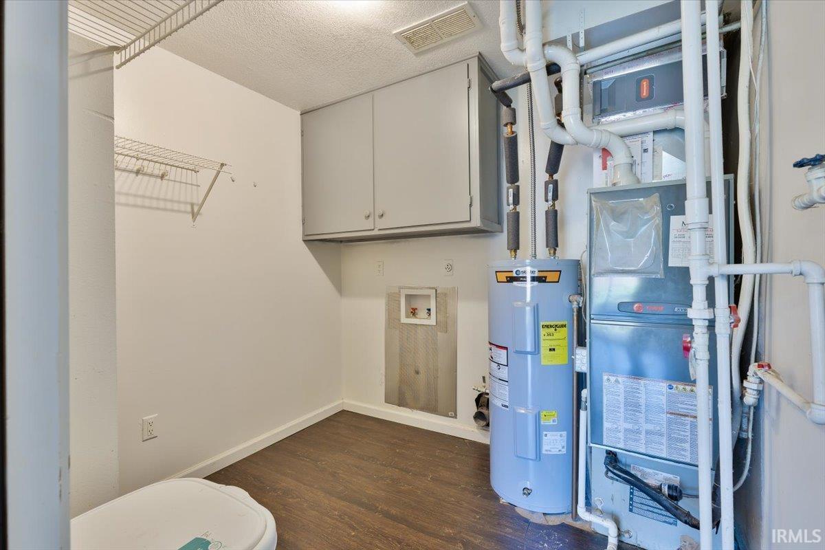 Dedicated utility area featuring a water heater, furnace system, and wood-finish flooring