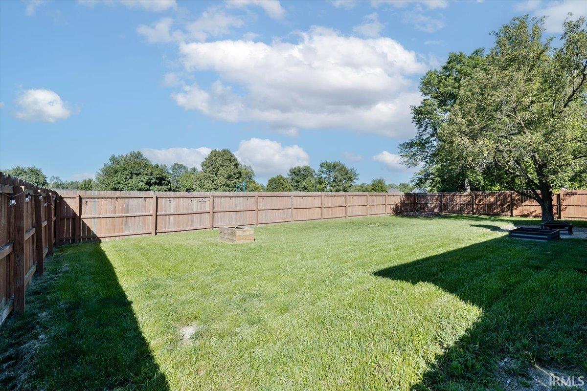 Expansive backyard featuring a large grassy area, full privacy fencing, mature trees, and a built-in fire pit