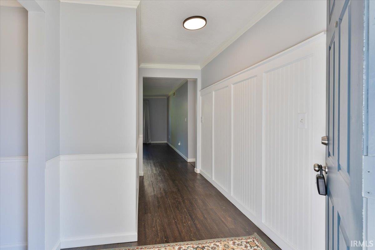 Entryway featuring dark wood-finish flooring, white beadboard wainscoting, light gray wall paint, white crown molding, and a flush-mount ceiling light fixture