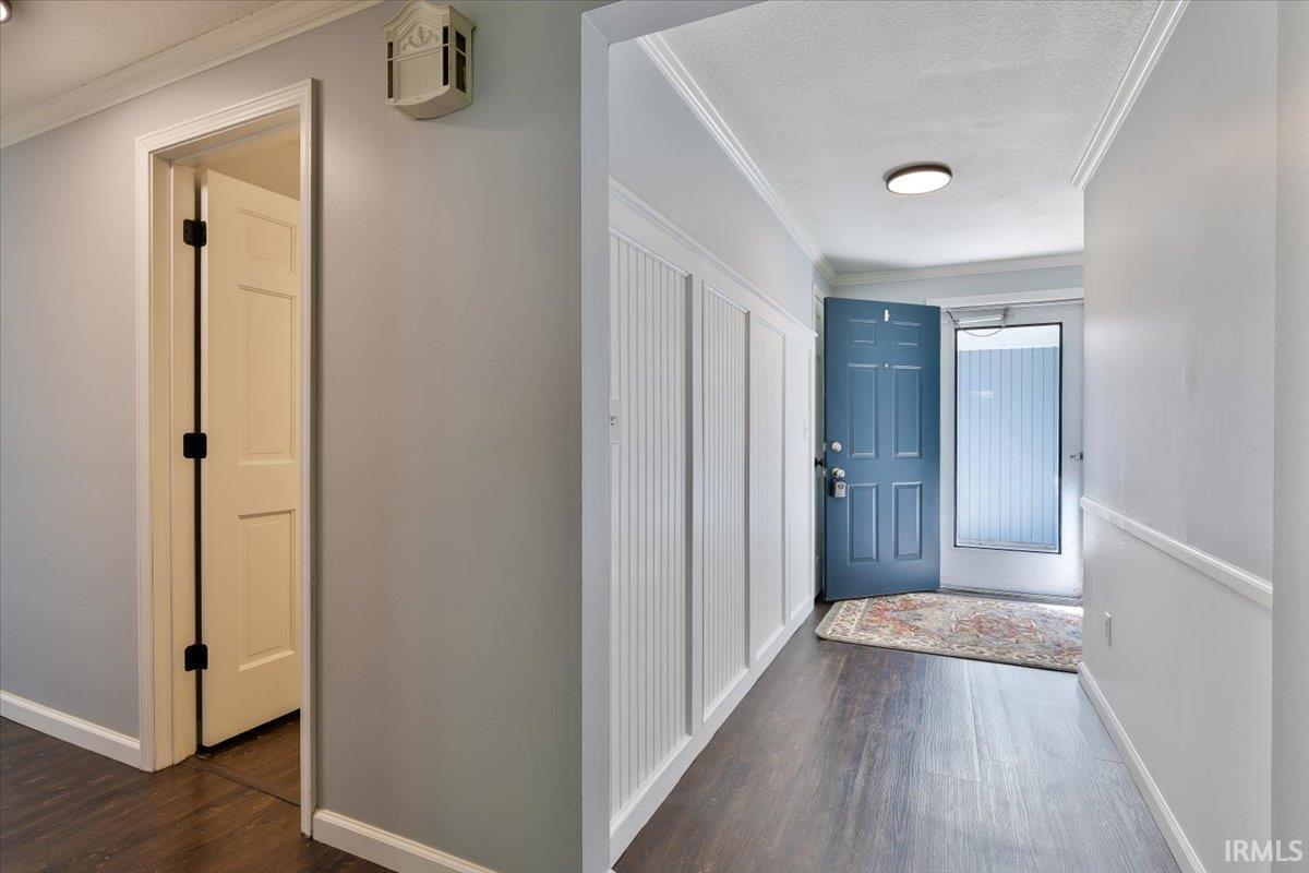 Entryway featuring wood-finish flooring, white wainscoting, and crown molding