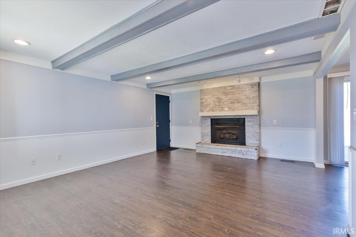 Spacious room featuring wood-finish flooring, a stone-accented fireplace, and a beamed ceiling with recessed lighting