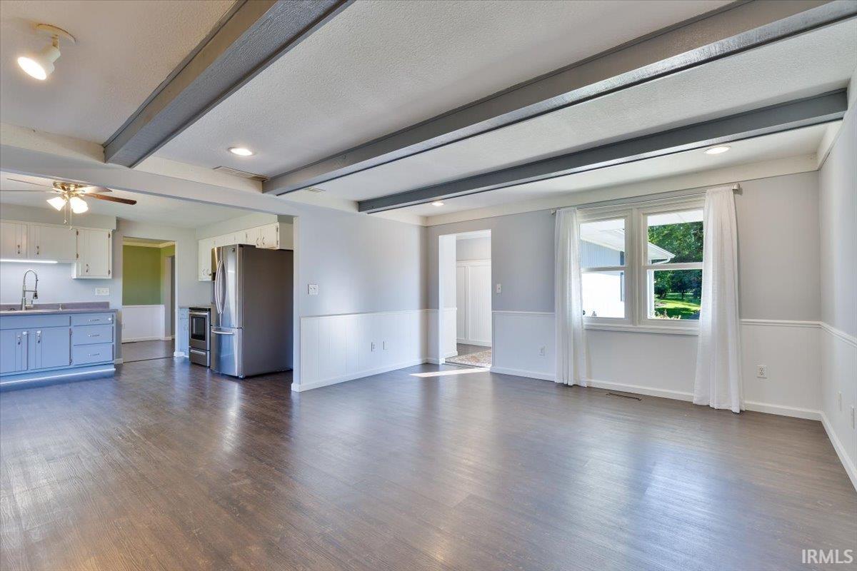 Expansive living area featuring exposed ceiling beams, wood-finish flooring, and wainscoting